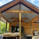 Covered patio with exposed wood beams, corrugated metal ceiling, and open posts before Mountain View Screens installation.