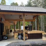 Wide view of covered patio with hot tub, outdoor seating, and wood post framing before screen installation.