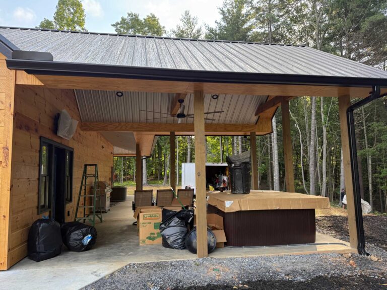 Wide view of covered patio with hot tub, outdoor seating, and wood post framing before screen installation.
