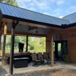 Side angle of covered patio with black metal roof, wood posts, and open layout before screens are installed.